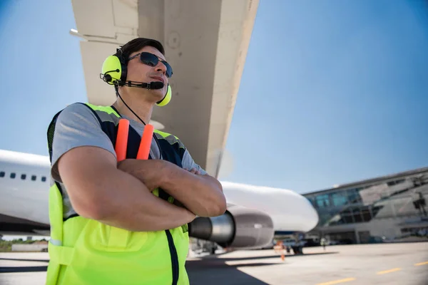 Trabajador de aeropuerto en gafas de sol y auriculares cruzando brazos — Foto de Stock