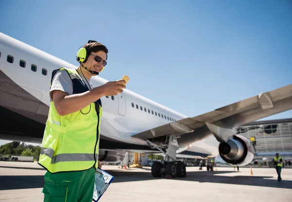 Веселий працівник аеропорту читає повідомлення на мобільному телефоні — стокове фото