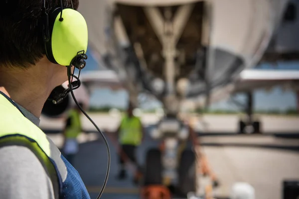 Airport worker in headphones looking at colleagues near passenger plane