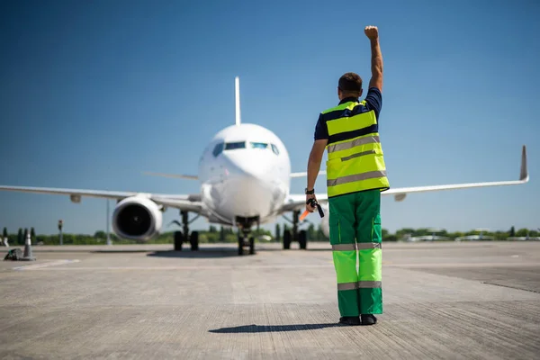 Працівник аеропорту піднімає руку і направляє пасажирський літак у правильному положенні — стокове фото