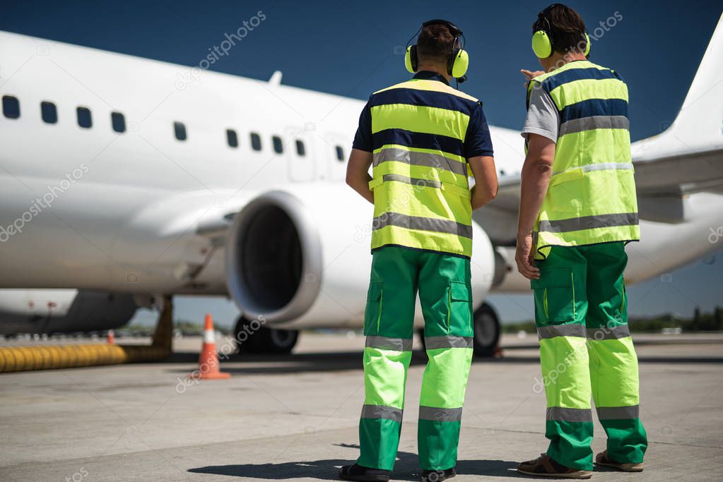 Airport workers looking at plane and discussing departure