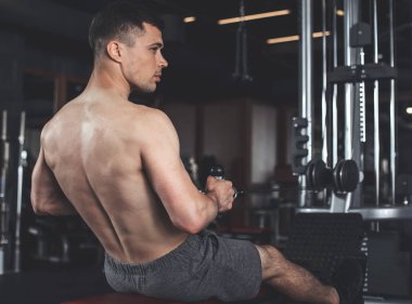 Rendelenmiş gömleksiz adam yatay sıra makine kapalı kullanıyor. O oturan ve kolları çekerek. Adam kıyafeti ve güç ve rahatlama için ağır ağırlık ile eğitiyor