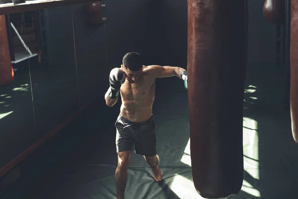 Báječný člověk naráží boxovací pytel ve sport studiu — Stock fotografie