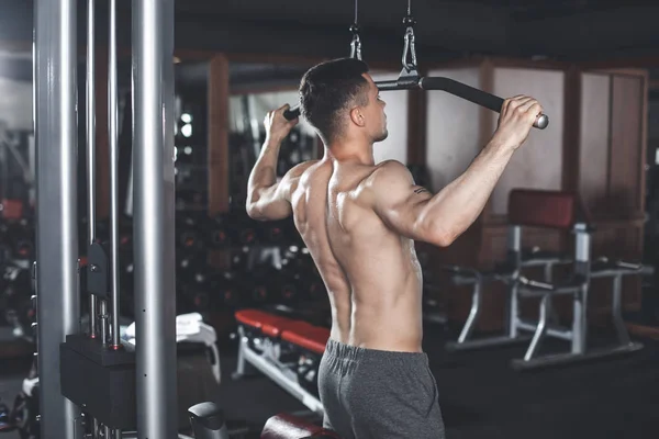 Masculino está treinando de volta com máquina no ginásio — Fotografia de Stock