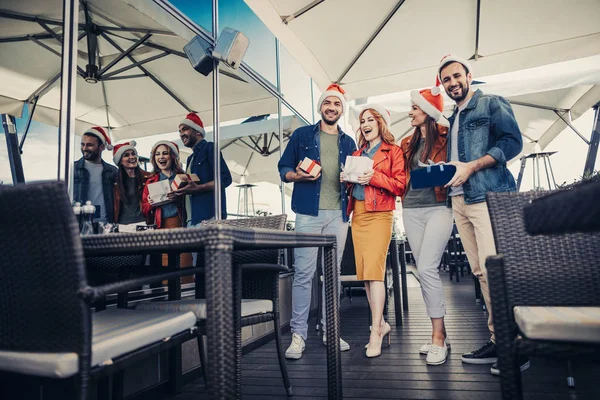 Veselá vousatých mužů a krásné dámy v Santa Claus klobouky hospodářství dárky — Stock fotografie