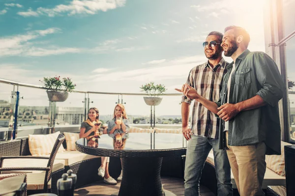 Веселі бородаті чоловіки спілкуються в той час як милі молоді дами насолоджуються алкогольними напоями — стокове фото