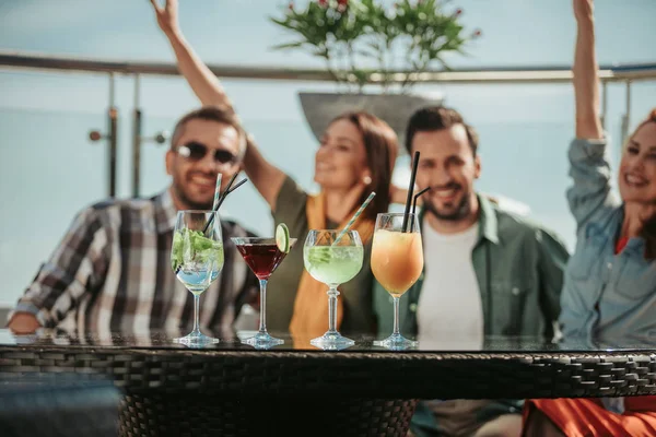 Various cocktails on table with cheerful friends on blurred background