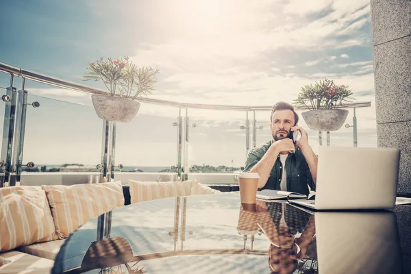 Hombre barbudo serio hablando por teléfono celular mientras está sentado en la cafetería al aire libre — Foto de Stock