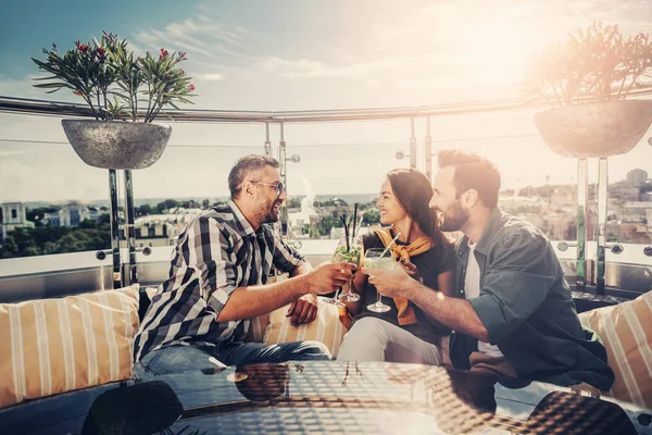 Tres amigos sonrientes en la cafetería de la azotea con cócteles — Foto de Stock