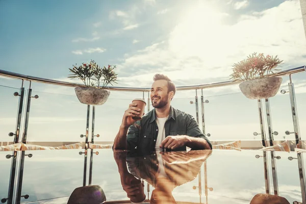 Glad man med kopp varm dryck sitter vid café bord — Stockfoto