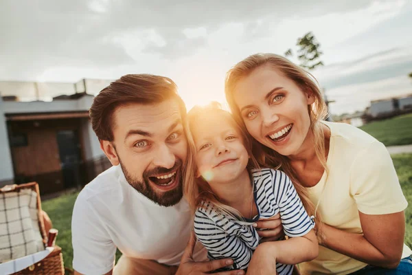 Pareja feliz abrazando a su hija optimista durante el atardecer — Foto de Stock