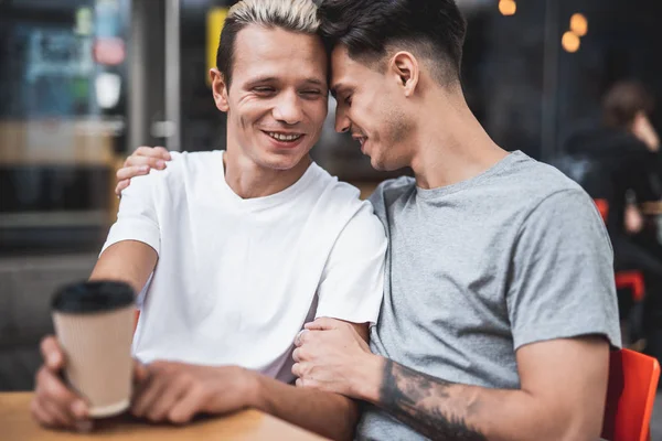 Lächelnder Kerl umarmt fröhlichen Freund am Tisch — Stockfoto