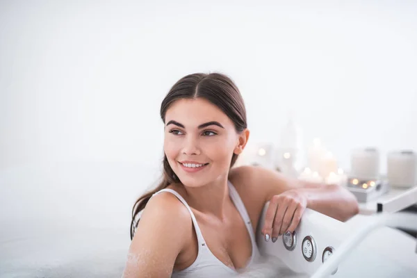有魅力的女孩的肖像在浴缸边上倚着迷人的微笑 而有泡沫水的水疗处理程序 — 图库照片