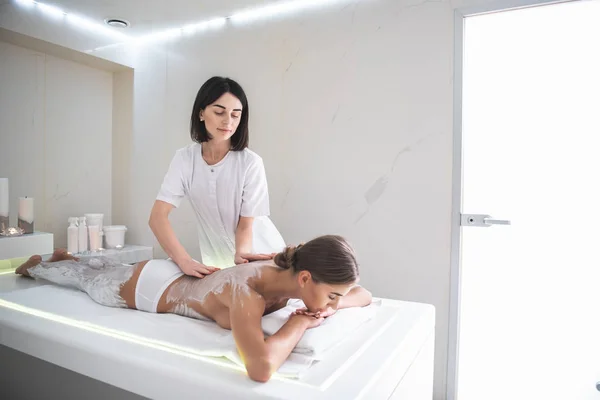 Young masseur doing spa procedure with white clay — Stock Photo, Image