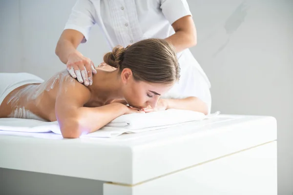 Serene young lady having back massage with white clay — Stock Photo, Image