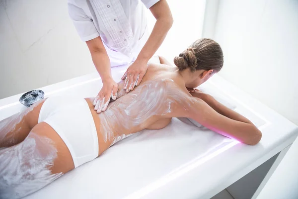 Massagista fazendo massagem com barro branco na menina de volta — Fotografia de Stock