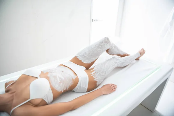 Female slim body on massage table with cosmetic mask on legs and belly — Stock Photo, Image