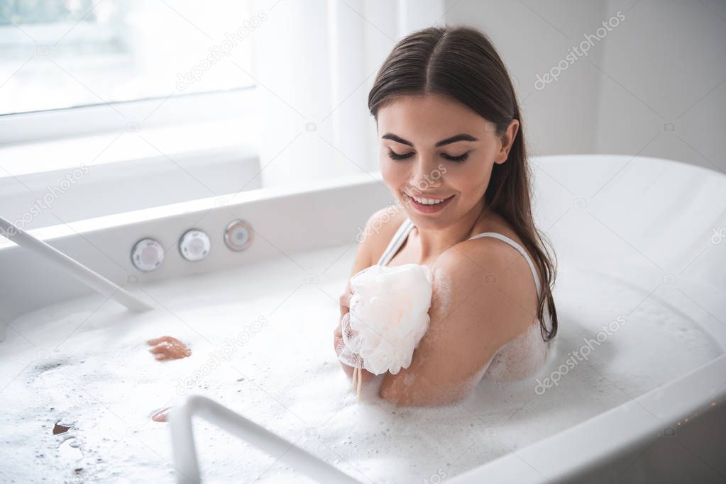 Pleased female washing body with shower sponge