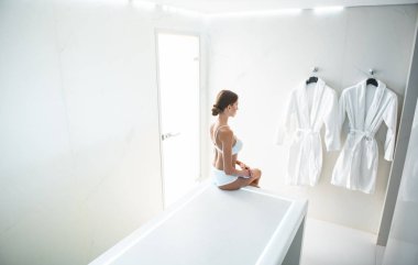 Sevimli genç kadın beyaz iç çamaşırı ve duvardaki yumuşak bornozlar