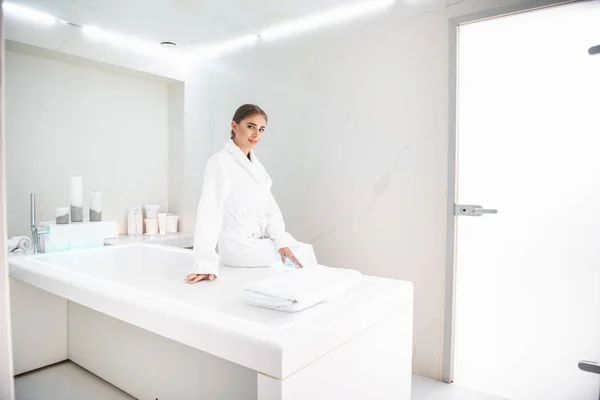 Attractive young woman sitting on massage desk at beauty salon — Stock Photo, Image