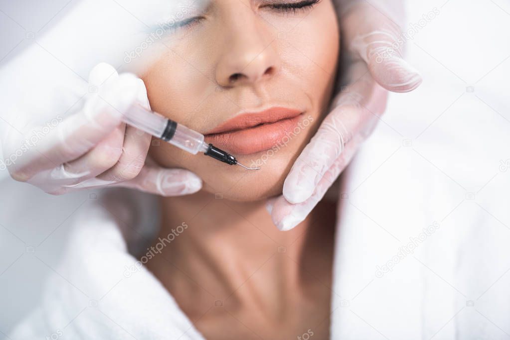 Beautician hands holding girl face and making injection to chin