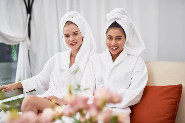 Usmívající se dívky s ručníky na hlavách sedí na gauči — Stock fotografie