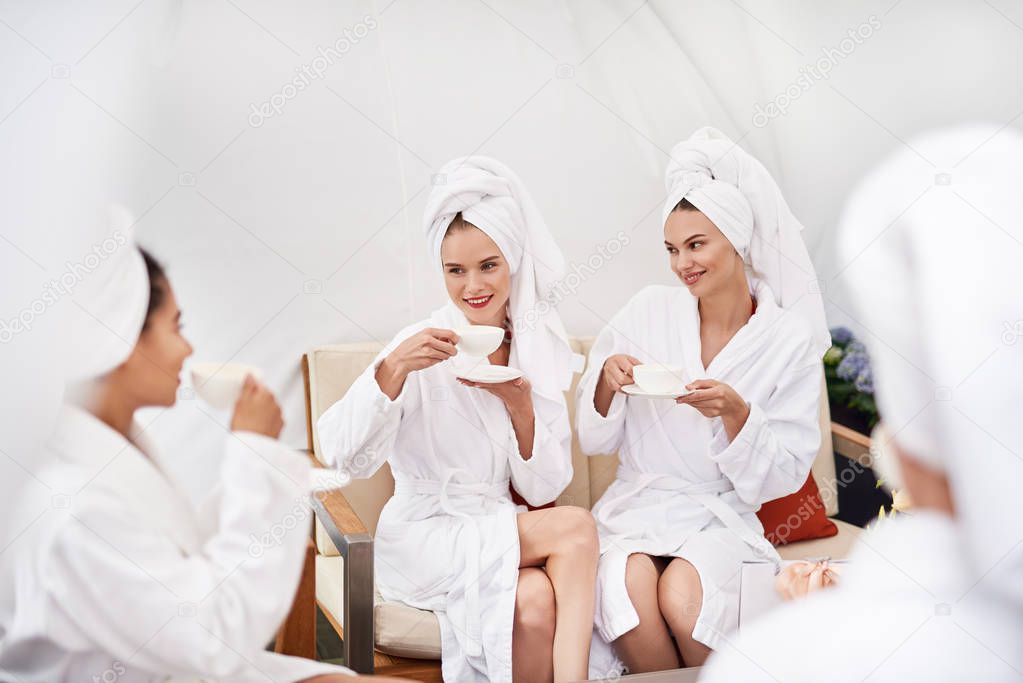 Charming girls enjoying tea and chatting at spa lounge