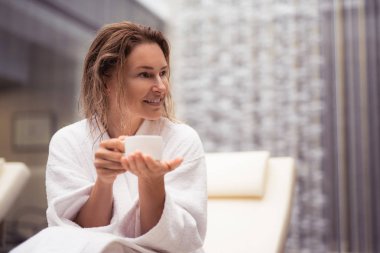 Beyaz bornoz favori sıcak içecek fincan tutan güzel orta yaşlı Bayan