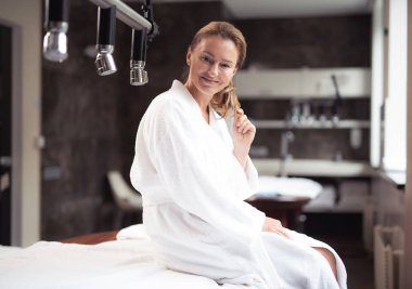 Spa salonunda daybed üzerinde oturan neşeli orta yaşlı kadın