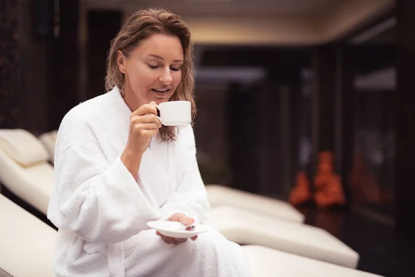 Glimlachend midden leeftijd vrouw in witte badjas genieten van koffie — Stockfoto