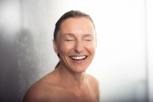 Красива жінка середнього віку приймає душ і сміється — стокове фото