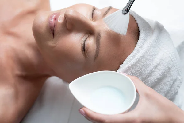 Affascinante signora con asciugamano sulla testa ricevere trattamento di cura della pelle al salone spa — Foto Stock