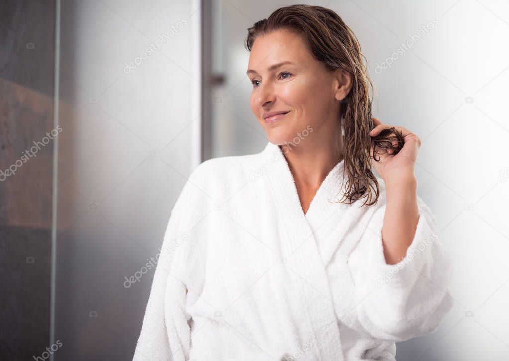 Happy middle aged lady standing near bathroom after taking shower