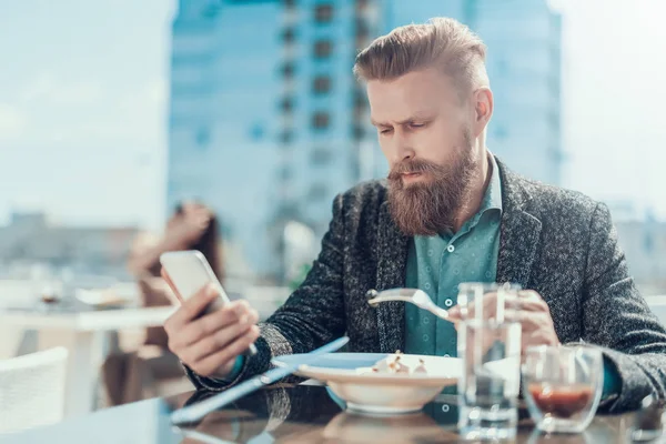 Hombre serio sin afeitar mirando en el móvil fuera — Foto de Stock