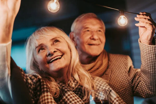Счастливая улыбающаяся пожилая пара смотрит на гирлянду — стоковое фото