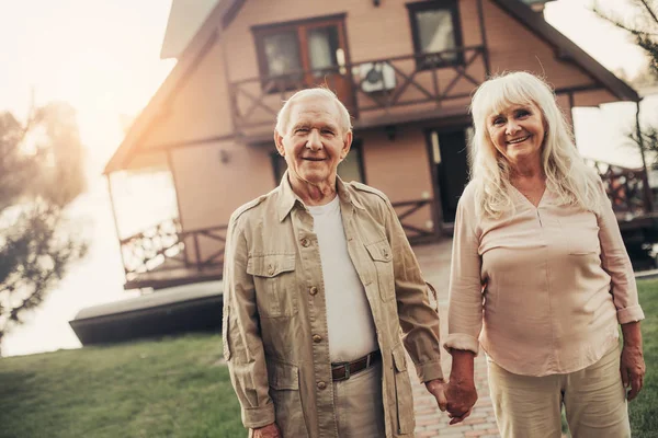 Feliz sonriente pareja de ancianos cerca de pequeña casa de campo — Foto de Stock