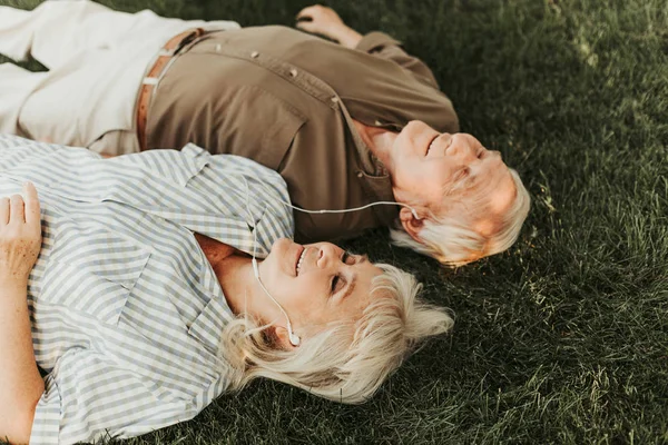 Joyous aged pair relaxing with music in earphones — Stock Photo, Image