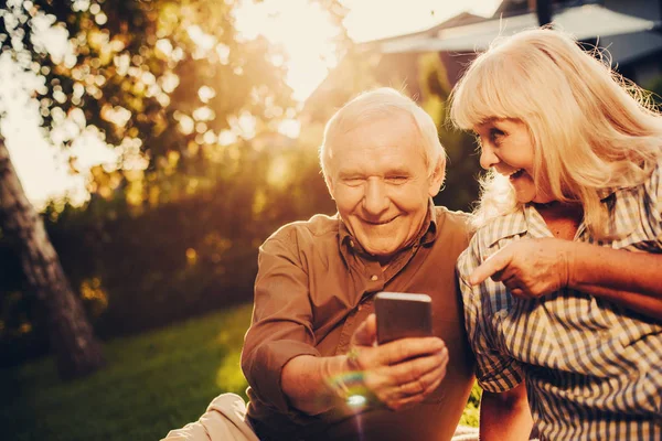 Веселая улыбающаяся пожилая пара, пользующаяся смартфоном на открытом воздухе — стоковое фото