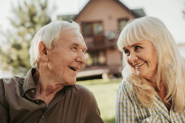 Lyckliga gamla paret sitter på gräsmattan som vetter mot hus — Stockfoto