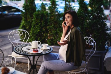 Büyüleyici hamile kadının Smartphone'da açık kafede konuşuyor