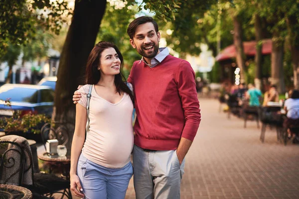 Bebaarde man knuffelen zijn charmante zwangere vrouw en op zoek weg met glimlach — Stockfoto