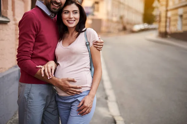 Glücklicher bärtiger Mann umarmt seine charmante schwangere Frau auf der Straße — Stockfoto