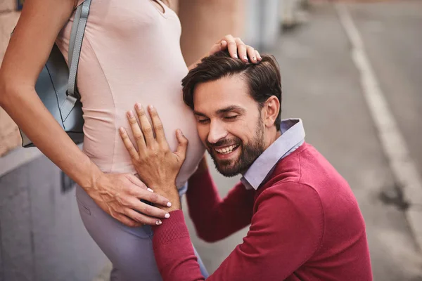 ひげを生やした男の美しい妊娠中の妻のおなかに耳を傾け笑みを浮かべてください。 — ストック写真