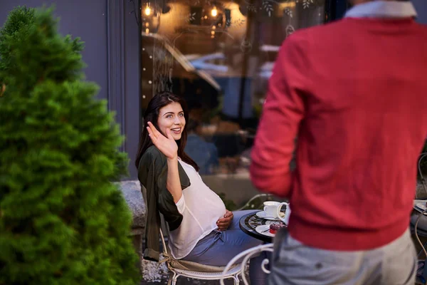 Beautiful pregnant lady sitting at the table and waving hand to husband — Stock Photo, Image