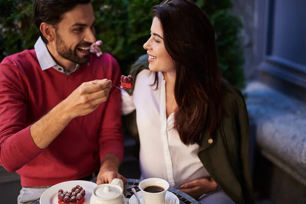 Cheerful bearded man holding spoon with cake and looking at his pregnant wife — Stock Photo, Image