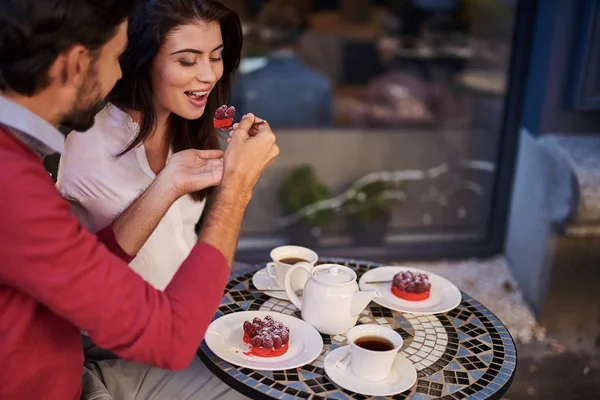 Bearded man feeding his charming girlfriend with spoon of tasty cake — Stock Photo, Image