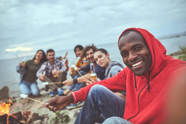 Guy fritando marshmallows com seus amigos na praia — Fotografia de Stock