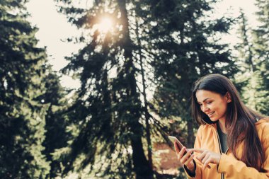 Çekici kız güneşli iğne yapraklı ağaç Smartphone kullanarak