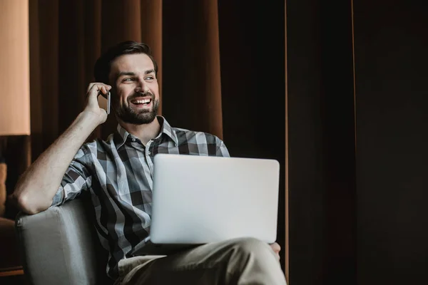 Homme joyeux parle au téléphone tout en utilisant un ordinateur portable — Photo