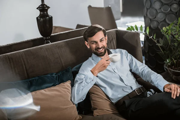 Homme d'affaires joyeux se détendre sur le canapé avec une boisson chaude — Photo